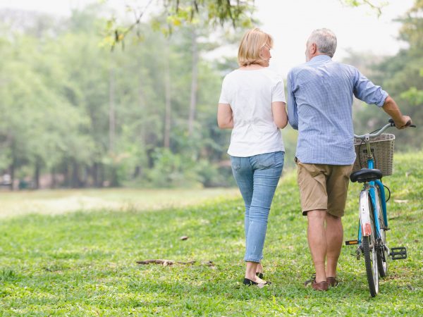 Elderly man and woman walking with a bike in a park